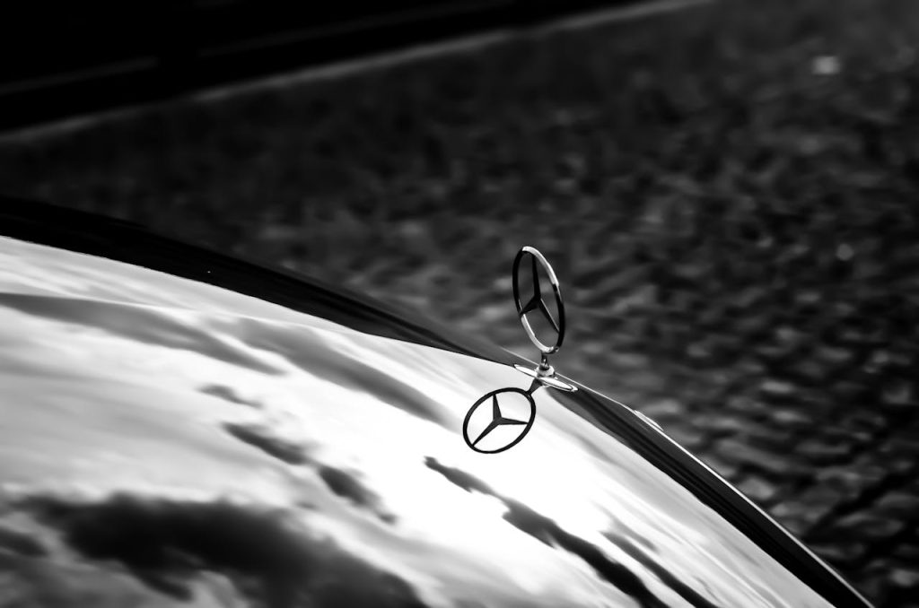Elegant black and white photograph of a Mercedes hood ornament reflecting on the cars hood.