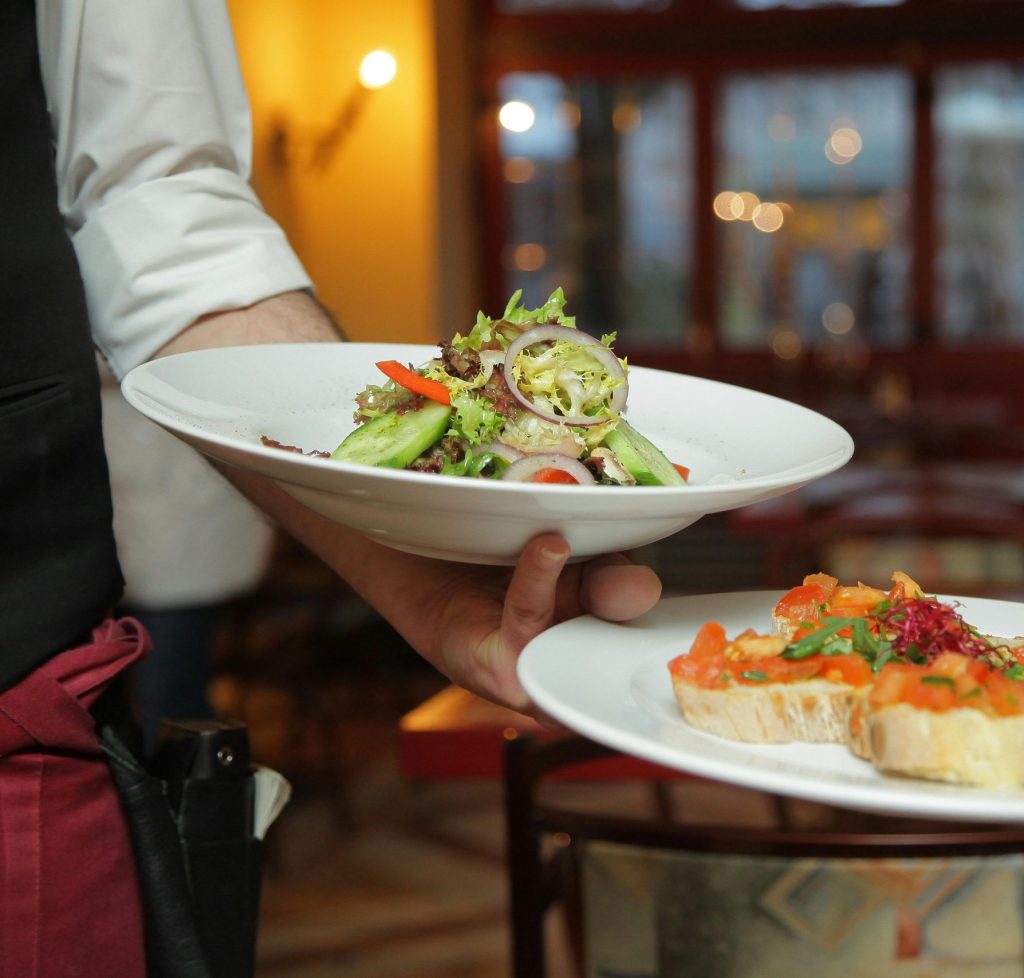A waiter serves a fresh salad and hors d'oeuvres in a cozy restaurant setting.